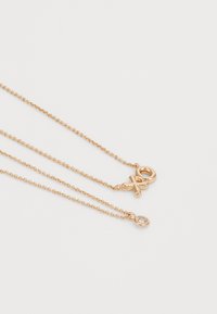 Collana a più strati in tonalità oro che presenta due catene delicate. Una catena ha un fermaglio rotondo; l'altra ha un piccolo pendente in pietra preziosa trasparente.