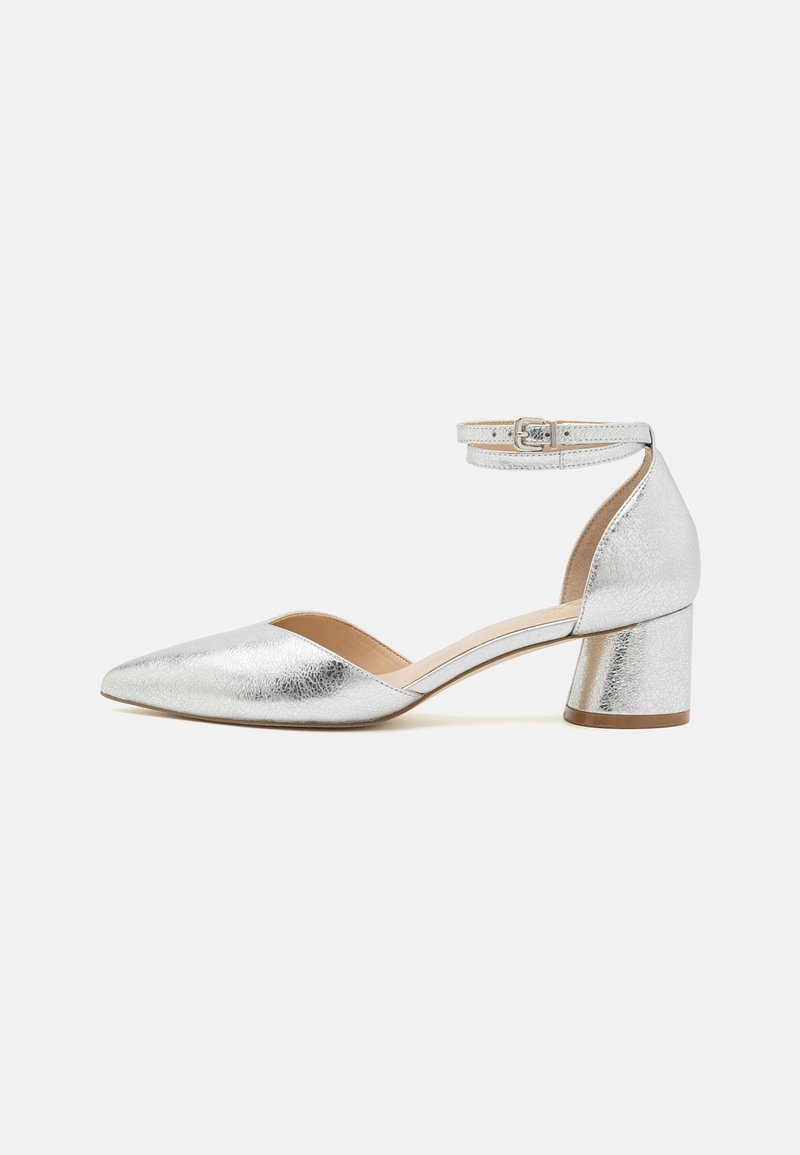 Chaussure argentée métallique à bout pointu, talon bloc bas avec bride à la cheville et boucle sur fond clair.