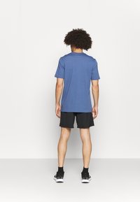 Camiseta azul de manga corta con escote redondo, combinada con pantalones cortos negros. La tela parece suave, con un corte holgado y un diseño minimalista.
