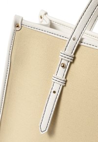 Beige Leinenshopper mit weißen Ledergriffen, mit schwarzem Nähten, Metallbeschlägen und kontrastierenden strukturierten Akzenten.