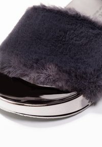 Fluffig, mörkgrå slide-sandal med en glänsande svart bas och metallisk silverdetalj längs kanten, med en mjuk, plädliknande textur.