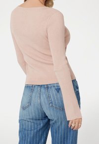 Top de manga larga acanalado color rosa claro con cuello redondo, combinado con jeans de mezclilla azul que presentan rayas blancas verticales y un bolsillo trasero.