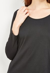 Must mustärgsed pikkade varrukatega pluus ümmarguse kaeluse ja pehme, sileda tekstuuriga, sobivate varrukatega, osaliselt õlavarre peal hoitud.
