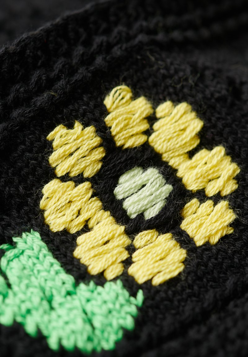 Schwarzer Stoff mit einem gelb-grünen gestickten Blumenmuster, das auffällige Blütenblätter und einen zentralen Punkt zeigt und mit strukturiertem Stich versehen ist.