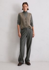 Szary golf pod beżową, teksturowaną kamizelką na guziki; zestawiony z szarymi, wzorzystymi, wysokim stanem spodniami i brązowymi butami.