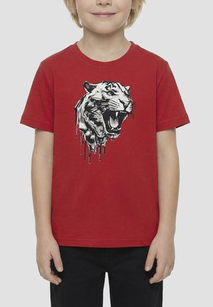 Kind draagt een rood T-shirt met een zwart-witte afbeelding van een brullende tijgerkop die lijkt te druppelen.