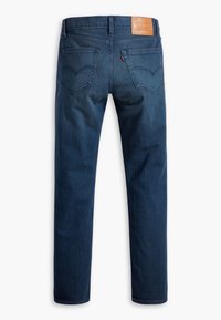 Jean droit bleu foncé vu de dos avec deux poches, détails de coutures, passants de ceinture et une étiquette de marque en cuir beige sur la ceinture.