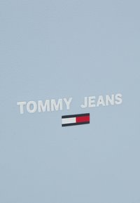 Superficie in finta pelle blu con il testo bianco "TOMMY JEANS" e un piccolo logo rettangolare con strisce rosse, bianche e nere.