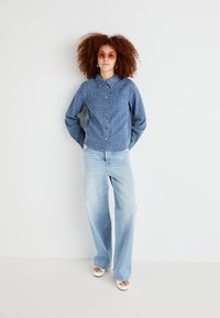 Blue patterned button-up shirt with a collar, paired with light-wash wide-leg jeans and white platform sandals, under soft lighting.