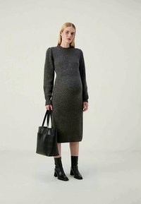 Vestido ajustado cinza escuro com mangas longas, textura canelada, até ao joelho. Combinado com botins pretos até ao tornozelo e uma mala tote preta.