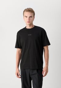 T-shirt en coton noir avec col rond, manches courtes et un subtil logo "BOSS" à l'avant. Texture lisse, coupe décontractée.
