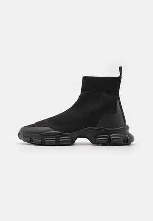 Czarne wysokie buty sportowe w stylu skarpetkowym z teksturowaną dzianinową cholewką, grubą segmentowaną podeszwą i pętelką na pięcie, widoczne z boku.