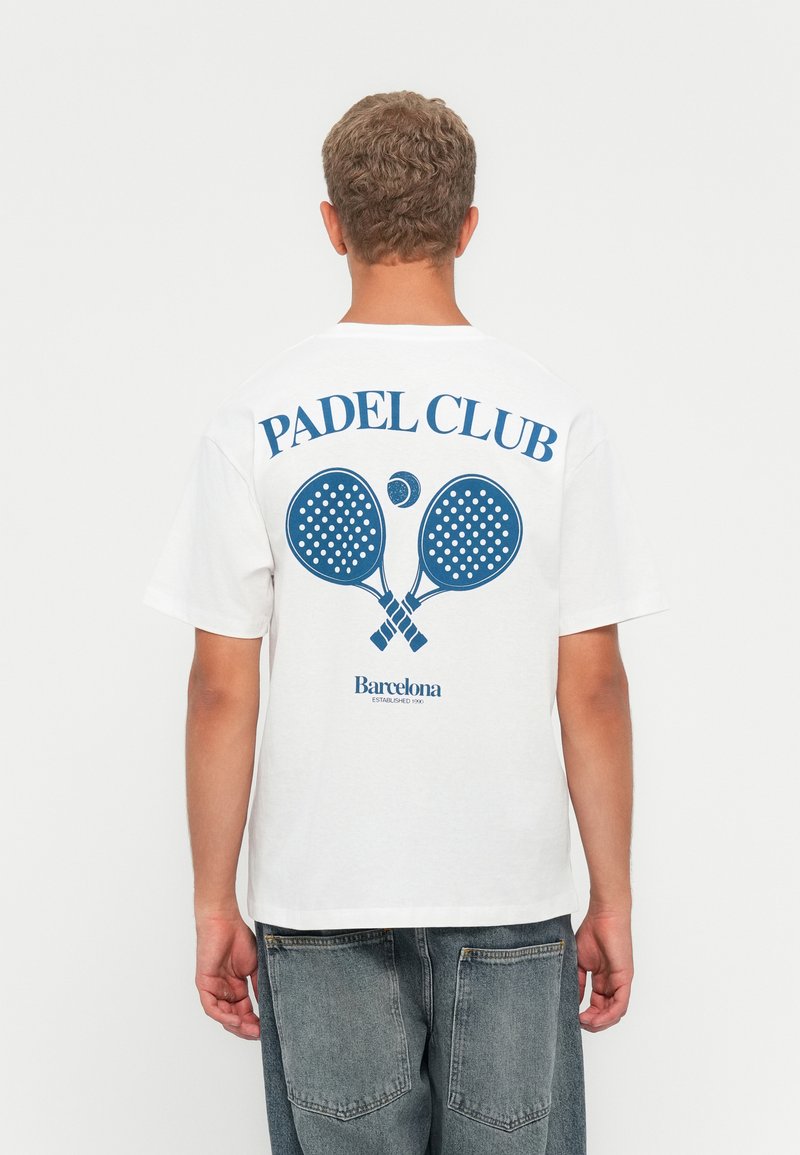 Hvit bomull t-skjorte med blå grafisk trykk på baksiden med "PADEL CLUB" og to padelraketter, samt "Barcelona"-tekst under.