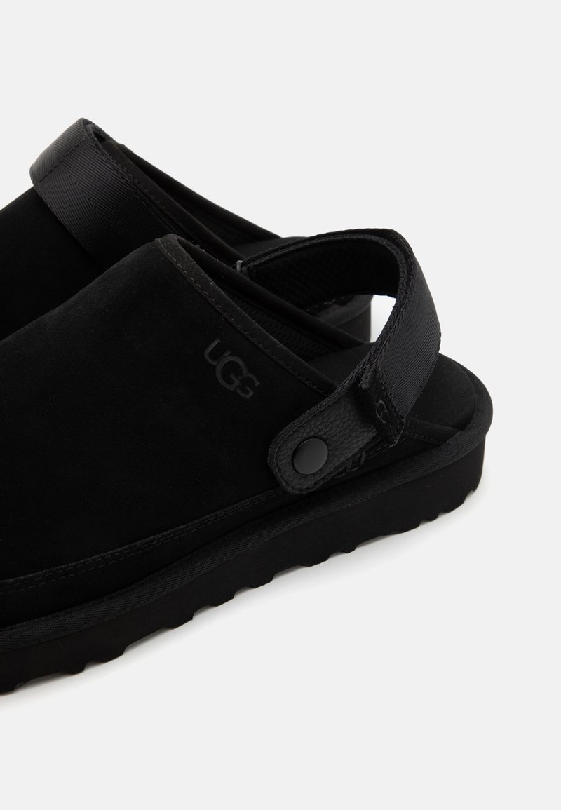 Scarpe slip-on in suede nero con una fascia testurizzata e un accento a bottone. Presentano una suola spessa per ammortizzazione e supporto.