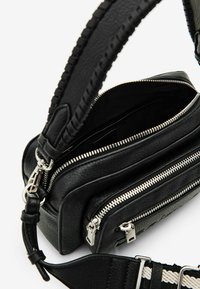 Svart lädercrossbodyväska med texturerad yta, utrustad med flera zipfack och ett mönstrat tygbärrem. Silverdetaljer.