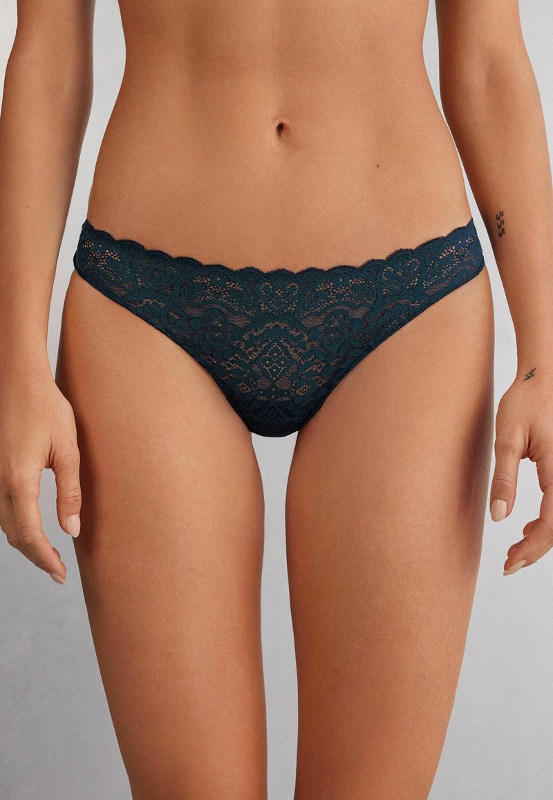 Kantenslips in diep teal met geschulpte randen. Bevat complexe bloemenpatronen en een delicate textuur. Lichtgewicht en aansluitend ontwerp.