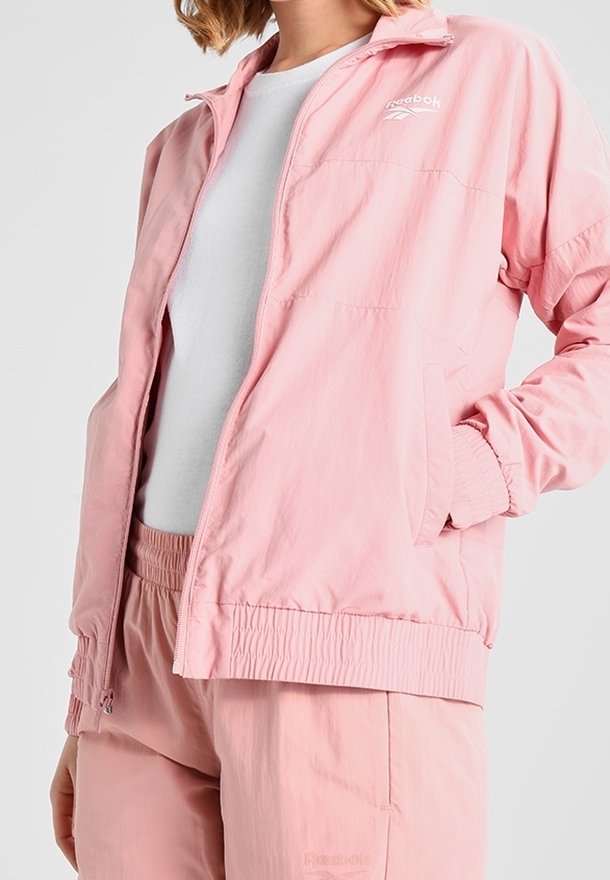 Light pink Reebok jacket with a zip front, elastic cuffs, and waistband. Made of smooth, lightweight fabric with a minimalist design.