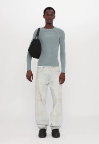 Lichtblauwe gebreide trui met lange mouwen en textuurpatronen, gecombineerd met losse crèmekleurige jeans met subtiele vlekken, en zwarte schoenen. Zwarte schoudertas.