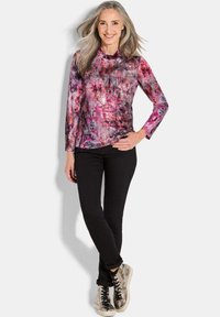 Multikleurige lange mouw top met abstracte roze en paarse patronen, gecombineerd met zwarte slim-fit broeken en metallic sneakers.