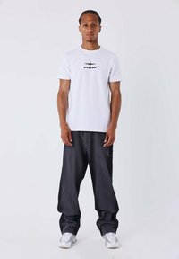 Camiseta blanca de manga corta con un logo negro "PXP", combinada con pantalones oscuros de corte holgado y zapatillas blancas. Diseño simple y limpio.