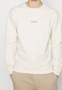 Cream sweatshirt made of soft fabric, featuring a round neckline, ribbed cuffs, and a small black "LES DEUX" logo on the chest.