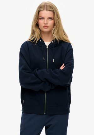 Felpa con zip color blu navy, con cappuccio regolabile e ampie tasche frontali, e polsini a costine. Tessuto morbido con una texture liscia.