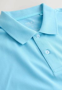 Polo bleu clair avec col et deux boutons, étiqueté « NEXT Regular Fit M », fabriqué au Bangladesh.