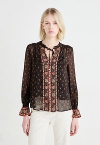 Blusa nera trasparente con ricami floreali, bottoni decorativi, colletto a cravatta e maniche a campana. Presenta un bordo a contrasto con motivo lungo la parte anteriore.