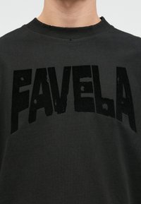 Černé bavlněné tričko s výrazným, opotřebovaným grafickým nápisem "FAVELA" na přední straně. Klasický střih s kulatým výstřihem a mírně opotřebovanou texturou.