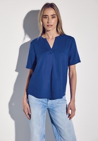 Blusa a maniche corte con scollo a V di un blu navy uniforme, realizzata in tessuto morbido. Abbinata a jeans azzurri chiari, leggermente vissuti.