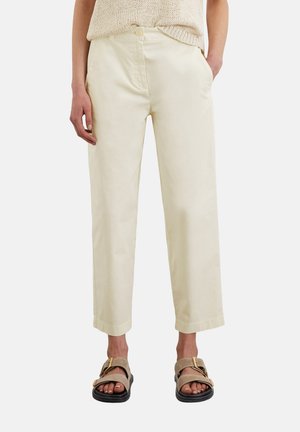 Lichtbeige katoenen broek met een rechte snit, twee zijzakken, een knoopsluiting en een iets cropped lengte. Draag met bruine sandalen.