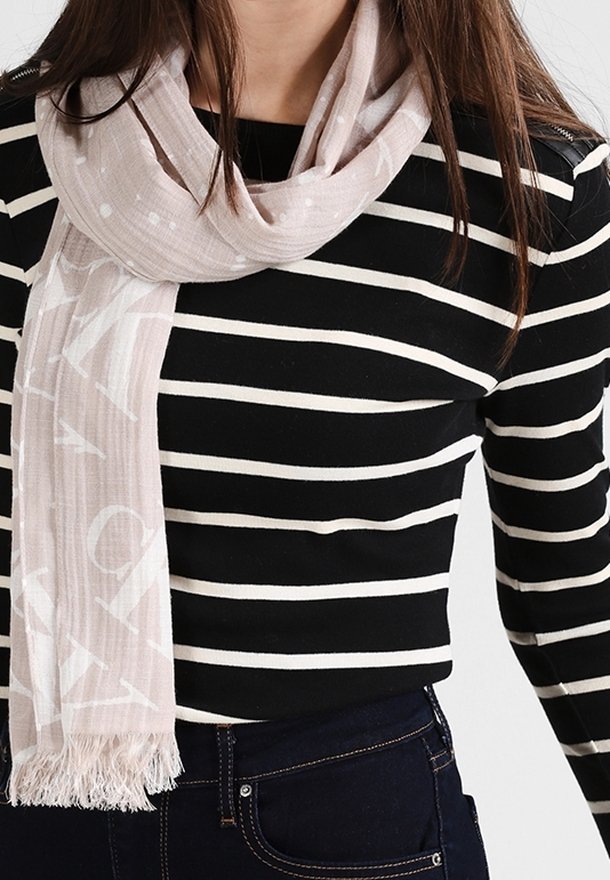 Femme portant un t-shirt à manches longues rayé noir et blanc et une écharpe claire avec des franges sur un jean foncé.