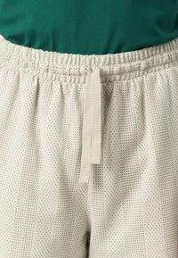 Pantaloni scurți de un bej deschis, cu o textură perforată, talie elastică cu cordon ajustabil și dungi verticale subtile.