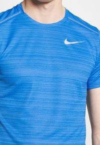 Blå atletisk t-shirt med texturerad väv och horisontella ränder, rund hals, och en vit Nike-logga på övre vänstra bröstområdet.