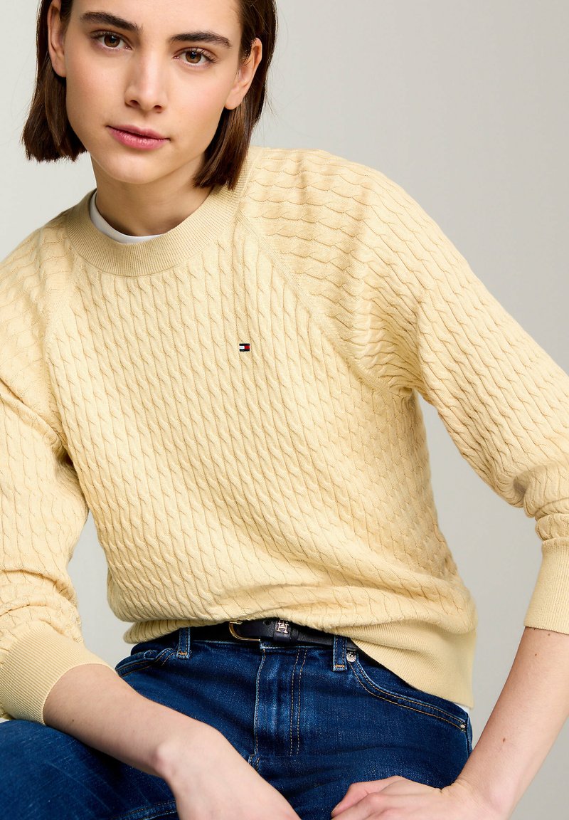 Kremowy sweter o dzianinowym splocie z fakturowanym wzorem w diamenty, okrągłym dekoltem i ściągaczami. Posiada małe logo na piersi.
