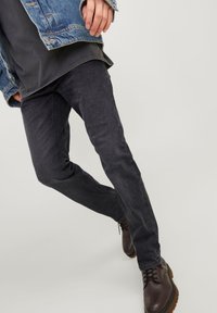Jeans slim fit em cinza escuro, feitos de denim, com desgaste sutil e design de cinco bolsos, combinados com botas castanhas de atacadores.