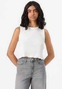 Top corto bianco a costine con orlo scallop e piccolo fiocco al colletto, abbinato a jeans in denim grigi ad alta vita.