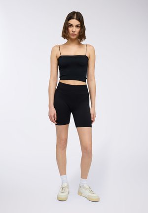 Top corto nero con spalline sottili e pantaloni bike neri a vita alta, entrambi in un tessuto liscio e elastico. Sneakers bianche e calzini alla caviglia.