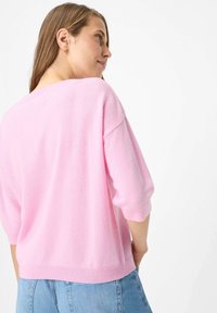 Pull rose doux avec une coupe ample, manches courtes et col arrondi. Associé à un jean en denim bleu clair.