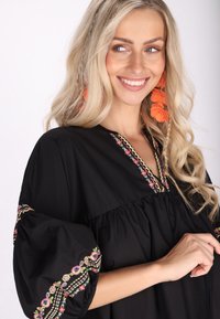 Bluză neagră cu mâneci scurte și puffate, având broderie florală colorată pe de-a lungul gulerului și marginile mânecilor. Textură de țesătură netedă.