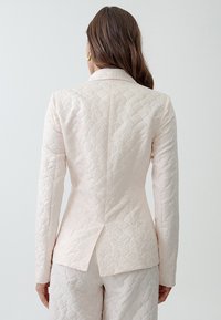 Light pink quilted blazer with a scalloped texture, single back vent, and tailored fit. Long sleeves and standard lapel design.