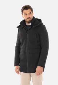 Cappotto invernale nero con cappuccio, chiusura a zip, tasche laterali e una texture morbida. Presenta una vestibilità ampia e un colletto, adatto per un abbigliamento casual.