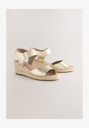 Kuldse metallilise viimistlusega kiilkontsaga sandaalid kahekordsete rihmadega, avatud varbaga ja punutud nöörpõhjaga. Siledapinnaline ja läikiva viimistlusega.