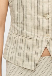 Veste en lin beige à rayures verticales marron, avec une fermeture à un seul bouton et une poche latérale. Tissu texturé avec une légère brillance.