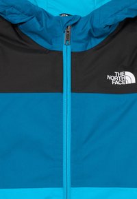 Καπιτόν κο jacket σε μπλε και μαύρο, με πλήρη μπροστινό φερμουάρ, αντίθετα πάνελ και το λογότυπο της The North Face στο στήθος.