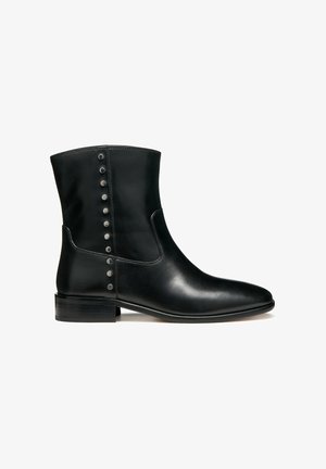 Botines de cuero negro con una textura suave, punta redonda y tacón pequeño apilado. Presentan tachuelas plateadas a lo largo del lateral como acentos.