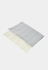 Tkany szary i biały koc o jodełkowym wzorze z kremowymi frędzlami wzdłuż jednego brzegu. Lekka i miękka tekstura. Prostokątny kształt.