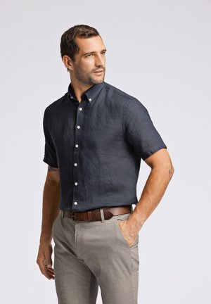 Korte mouwen, marineblauw linnen overhemd met een button-down kraag en witte knopen, gecombineerd met lichtgrijze op maat gemaakte broek en een bruine riem.