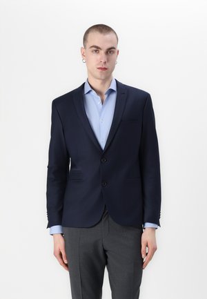 Blazer bleu marine à revers crantés, à deux boutons et avec poches avant, associé à une chemise bleu clair. Le tissu semble lisse avec une coupe ajustée.
