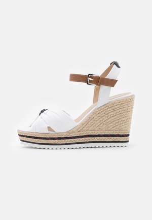 Sandale compensée en espadrille blanche avec tige en tissu noué, bride de cheville marron et talon compensé recouvert de jute texturée. Semelle en caoutchouc avec détails à motifs.